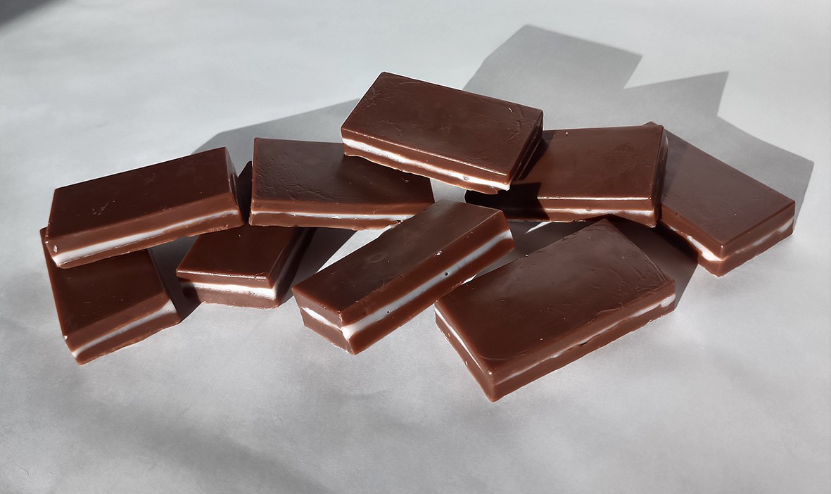 Brown soap chocolates with a pink strawberry layer made from soap base are placed on a white background.