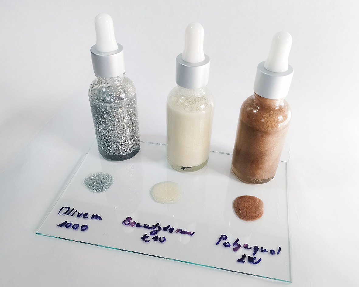 Tres tipos de aceites líquidos con brillo inmediatamente después de mezclarlos, en frascos de vidrio con cuentagotas. Los frascos y una plaquita acrílica transparente con gotas de los aceites sobre fondo blanco.