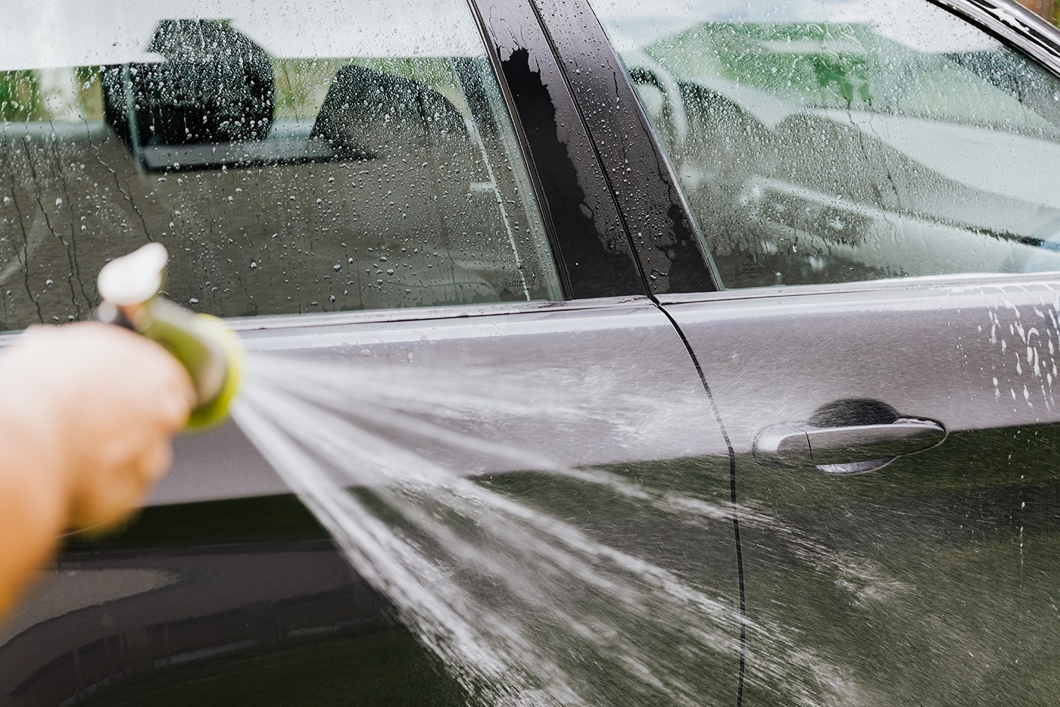 White vinegar can be used to clean car windows and to remove old stickers and adhesive. In the picture, a man is hosing the remaining vinegar off the side of the car.