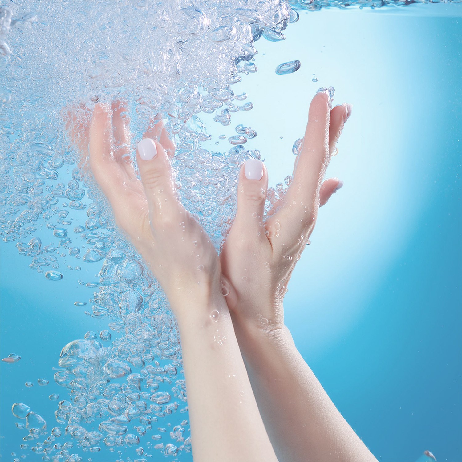 Vue de mains féminines dans l’eau, toute la photo a une teinte bleu pâle avec des bulles tout autour.