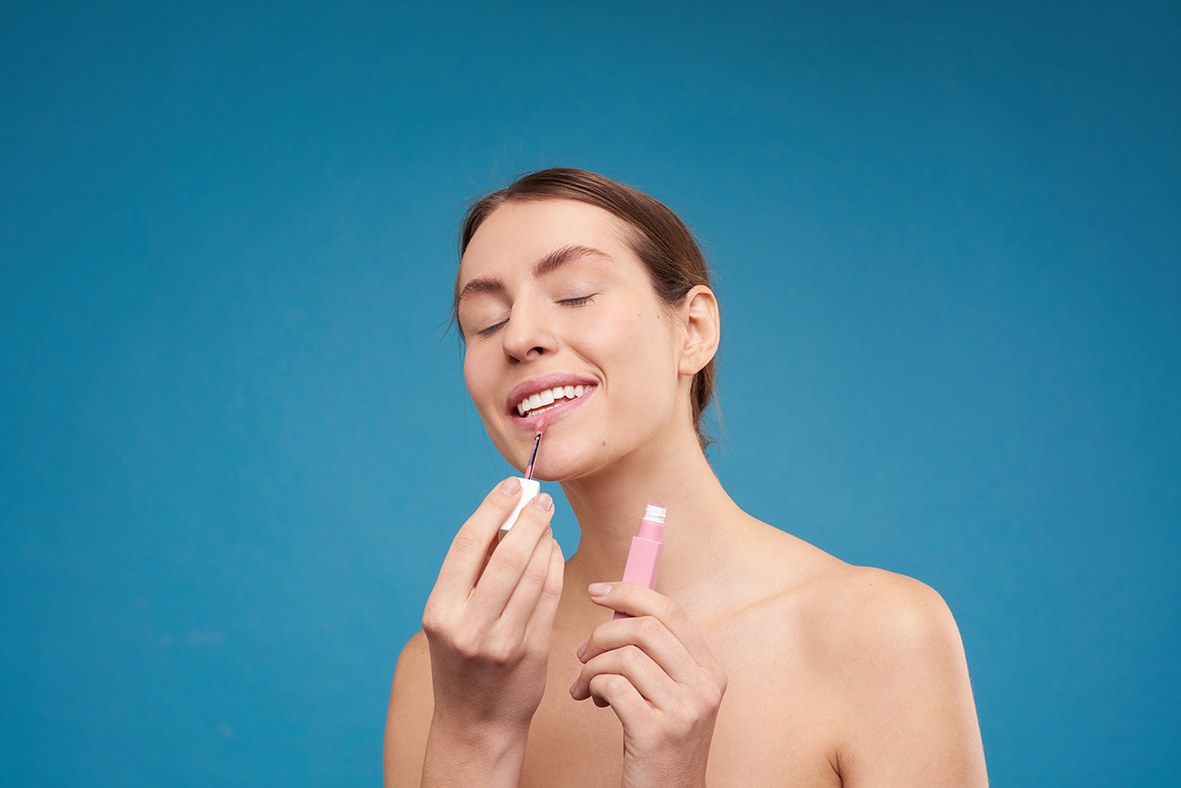 Una mujer se aplica en los labios un brillo de labios rosa elaborado con materias primas naturales.