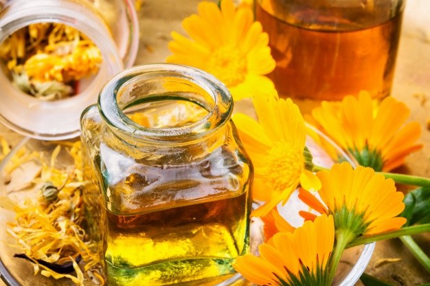 Frasco de vidrio con macerado y flores de caléndula.