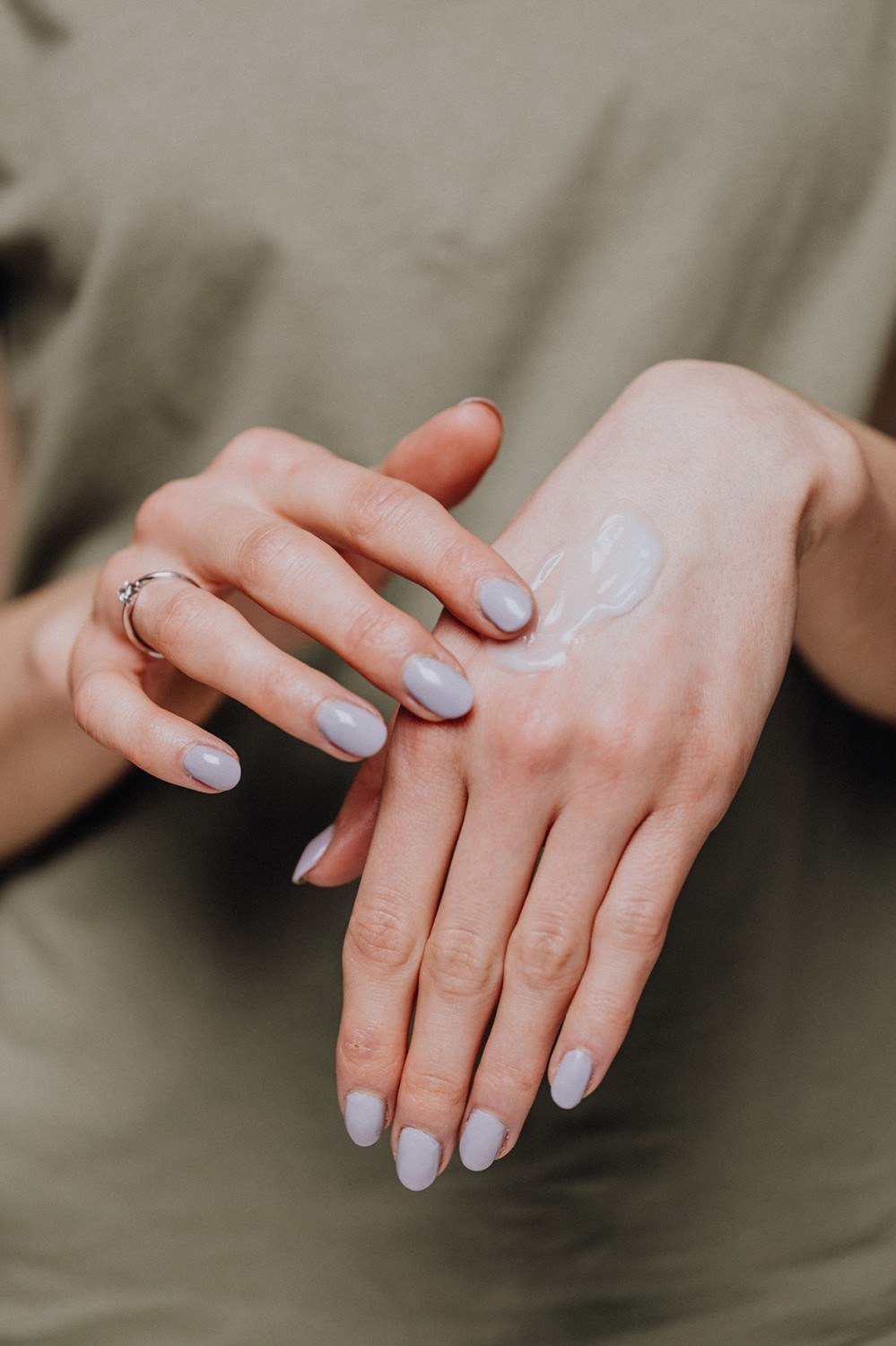 Eine Frau in grüner Bluse und mit grünem Nagellack verwendet eine Körperlotion aus natürlichen Rohstoffen.