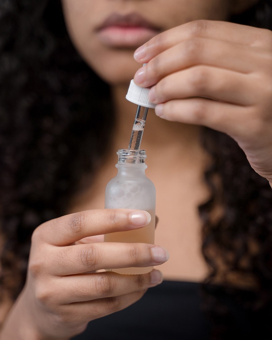 Serum do twarzy z minerałami w przezroczystej buteleczce z pipetą, trzymane w dłoniach przez kobietę.