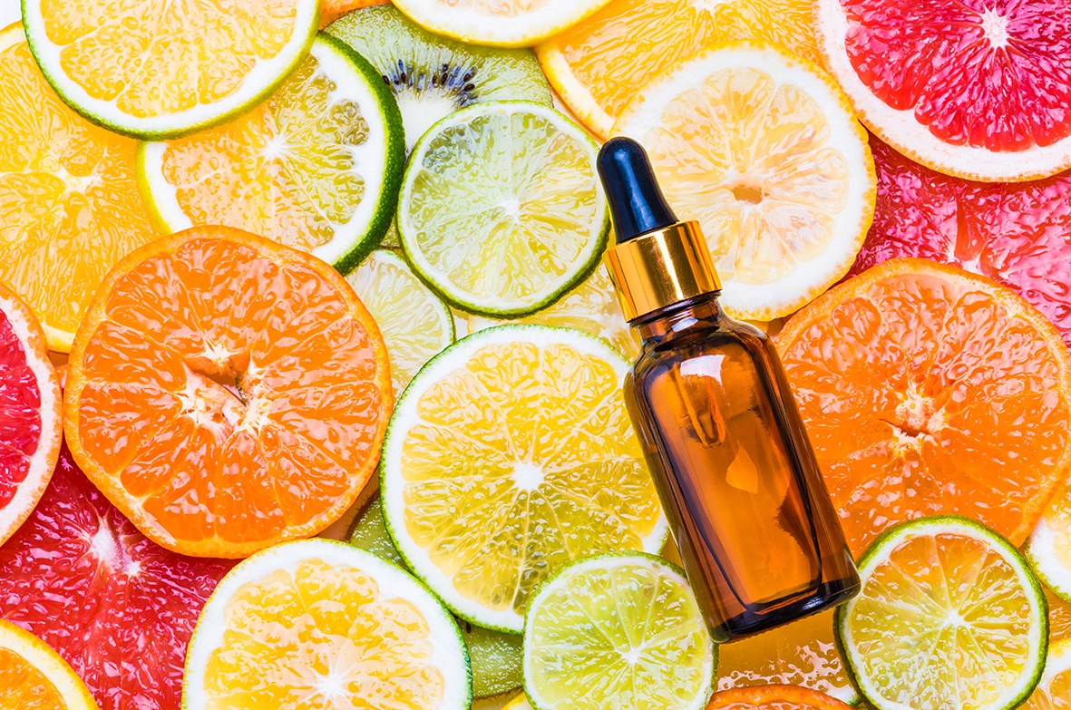 Sérum con vitamina C en un frasco de vidrio marrón con cuentagotas, apoyado sobre una superficie de cítricos cortados.