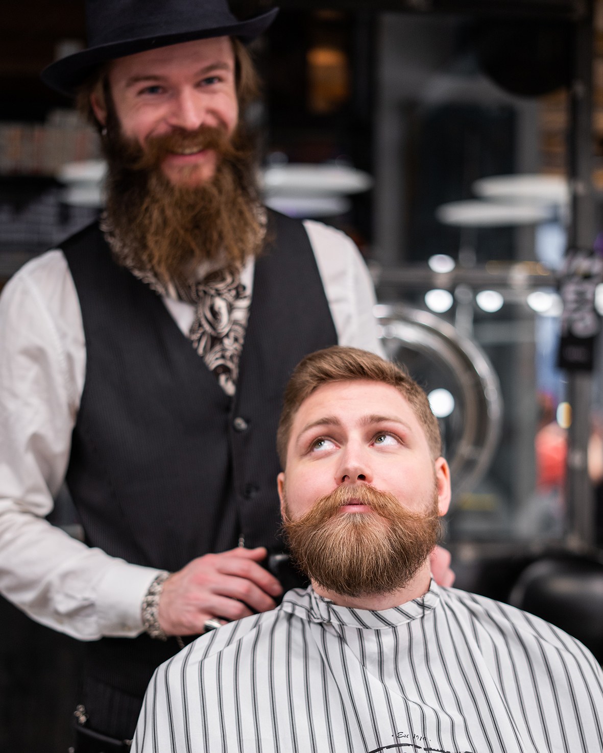 Klient u barbera siedzi w fotelu z brodą ułożoną za pomocą balsamu do brody. Za nim stoi jego fryzjer.